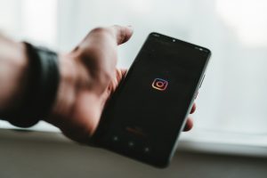 Photo d'une main d'homme tenant un téléphone portable avec le logo Instagram, illustration pour les conseils Instagram